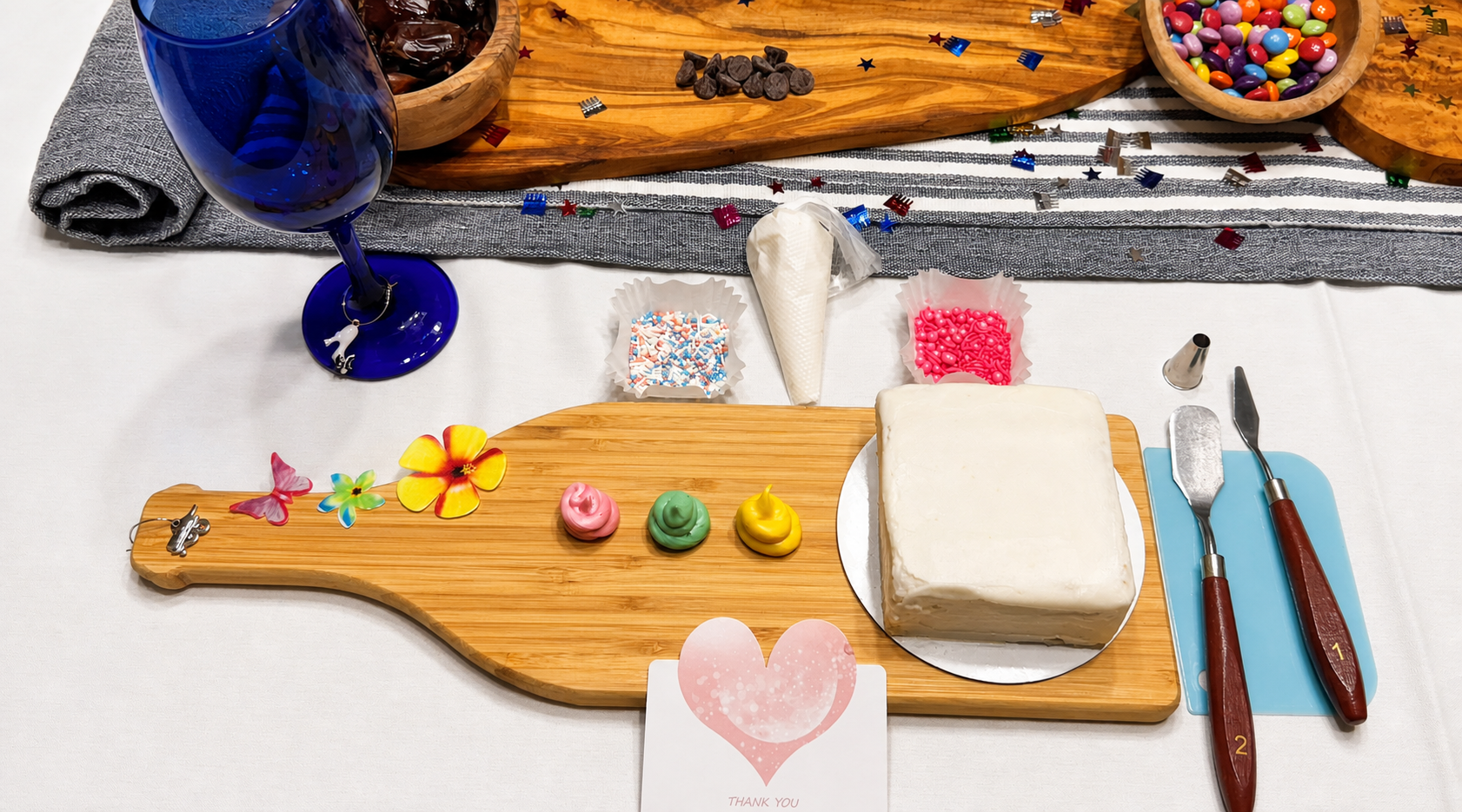 Cake and Sip decorating table prepared with a cake, frosting, sprinkles, and tools